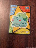 Front of a Pokemon Bulbasaur Topps sticker card showing colorful starburst background and Bulbasaur character.