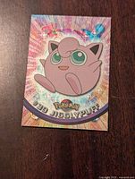 Front view of Pokemon Jigglypuff holographic trading card showing colorful glitter holographic background and character illustration.