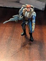 Front angle view of Dash Rendar Kenner action figure standing on wooden surface, showing details of figure and blaster accessory.