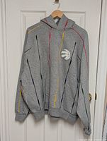 Front view of the grey men's hoodie sweater with multicolor stripes and Toronto Raptors logo patch on the left chest.