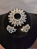 Brooch and earrings arranged on black display showing front view with sparkling rhinestones, demonstrating overall aesthetic and design.