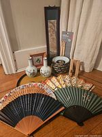 View showing four fans, two Famille Rose vases, black lacquer porcelain bowls, framed art, and wooden fan stand on hardwood floor.