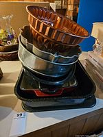 Stack of assorted baking pans including copper mold at top and cast iron casserole dish near bottom