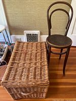 Vintage bentwood chair next to large rectangular wicker basket with lid on hardwood floor.