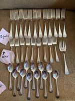 Top row displays 17 four-tine dinner forks arranged horizontally on sofa fabric
