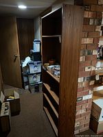 Side view of tall wooden bookshelf in basement showing shelves with items and scratches.