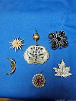 Six vintage brooches and pendants laid on blue fabric, showing variety of shapes and rhinestone detailing