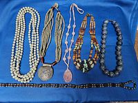 Top view of six costume jewelry necklaces displayed on blue fabric, showing necklace variety and colors.