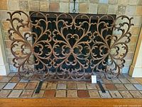 Full front view of ornate cast iron fireplace screen with scroll pattern and two support feet on tiled hearth