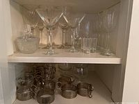 Shelving unit with clear glass cocktail glasses, wine glasses, shot glasses, and metal cup holders.