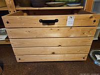 Front view of the pine wood storage crate showing natural wood planks and black handles.