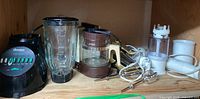 Shelf with multiple kitchen appliances including a black Osterizer blender, brown coffee maker or food processor, and handheld mixers with beaters and whisks.
