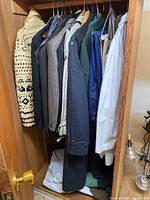 Photo of men's clothing items hanging in wooden closet showing sweaters, blazers, and jackets.