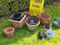 Plastic plant pots and crates arranged outside on grass, various sizes and colors, some stacked.