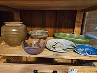 Shelf with various pottery pieces including vase, bowls, platter, green dish, two plates.