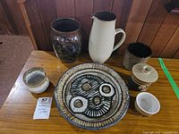Full display of pottery set including pitcher and five bowls with varying glazes and designs on wooden table.