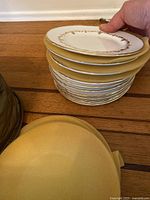 Stack of ten white Royal Worcester plates with gold decorative trim indicated by hand holding top plate to show design.
