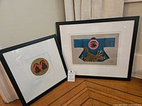 Photo showing both framed art prints together, one smaller and one larger, displayed against a wall and floor corner.