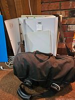 Photo showing several white plastic slide sorters/light-up slide viewers stacked against a wall with slide trays and a black portable carrying case in front.