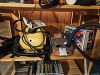 Photo showing vintage yellow Steam Buggy steam cleaner and electric air pump on a wooden shelf with hoses and attachments.