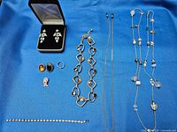Full lot of sterling and silver jewelry laid out on blue cloth, including earrings in black case, rings, bracelet, eyeglass chain, and necklaces.