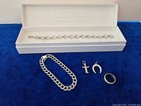 Photo of two bracelets, two charms and one ring all made of sterling silver placed on blue velvet with white box