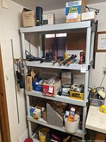 Four-level plastic shelf filled with assorted tools, hardware, wires, spray cans, and boxes.