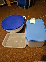 Photo showing four Tupperware containers in various shapes and lids, placed on the floor.