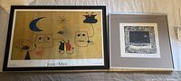 Two framed prints laid on a beige surface; colorful Joan Miró print on left and monochromatic signed print by Hauley on right.