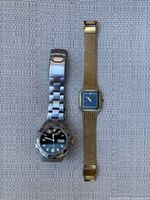 Two wristwatches on fabric surface: left is Pulsar men's sports watch with black dial and metal band, right is Seiko Lassale women's gold-tone square watch with mesh band.