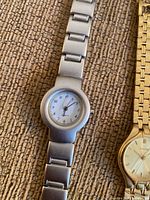 Four quartz wristwatches on carpet with metal bands, various colors and styles.