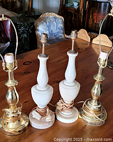 Four assorted lamps on wooden table, two marble and two metal with cords coiled around bases.