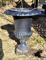 Front view of cast iron urn positioned outdoors on grass, showing detailed rim and tapered body.
