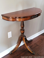Front angle of half-moon shaped wood console table with pedestal base and claw feet placed against wall.