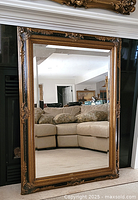 Full view of large rectangular mirror leaning against a wall, reflects a sectional sofa and room interior