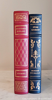 Side view of the red and black leather-bound books showing their spines with gold decorations and titles.