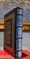 Front angle view of the dark blue leather bound book with gold gilt decoration and raised spine hubs.