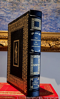 Side view of the leather bound book The Confessions of Saint Augustine showing the black leather cover with gold decorations and raised spine hubs.