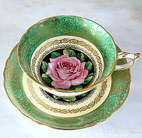 Cup and saucer set top view showing green and gold filigree and central pink rose motif