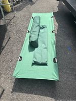 Green camping cot laid flat on ground showing the full cot and two green carrying bags on top.