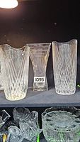 Three large glass crystal vases displayed side-by-side. Center vase is identified as Mikasa, with clear glass and stepped linear pattern. Two outer vases have textured vertical ribbed and diamond cut patterns. Clear lighting to show transparency and details.