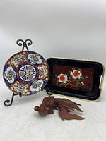 View of the porcelain plate with metal stand, black floral tray, and wooden koi fish figurine.