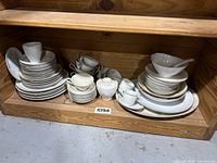 Full view of stacked plates, cups, bowls, creamer, and sugar bowl in wooden shelf showing the entire china set.