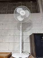 Full view of the Pelonis standing fan on adjustable stand against a gray wall.