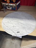 Top view of the round marble table top showing white marble with gray veins and label 899 attached.
