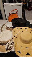 Overview of five ladies hats and an orange vintage handbag arranged on a surface for display.