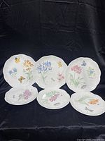 Front view of six Lenox Butterfly Meadow plates showing varied floral and butterfly designs on white porcelain with scalloped edges.