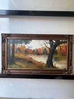 Full view of the framed oil on canvas landscape painting showing fall trees and a pond.