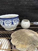 Photo showing three items: large blue and white ceramic planter, small gray planter, and large shell-shaped garden decoration on a metal rack.