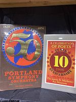 Both posters side by side showing full view of the Portland Symphony 50th Anniversary poster and the framed Michener Art Museum poets anniversary poster.